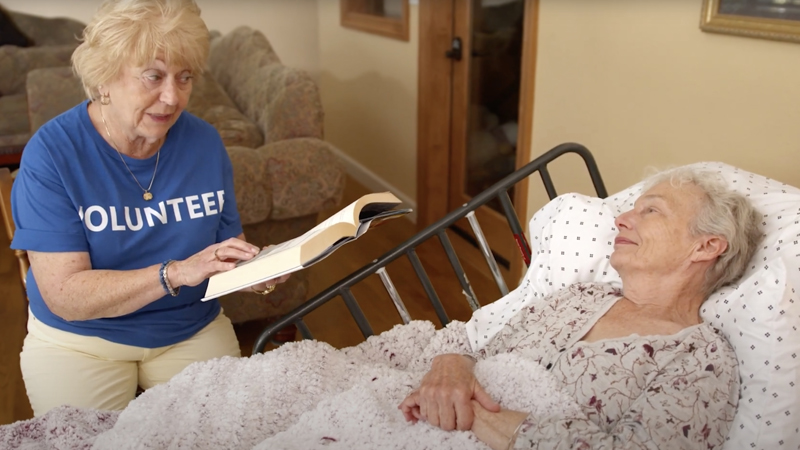Woman reading a book to an elderly woman in bed